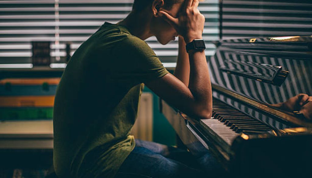 Teenager sitting at his piano with his head in his hands.