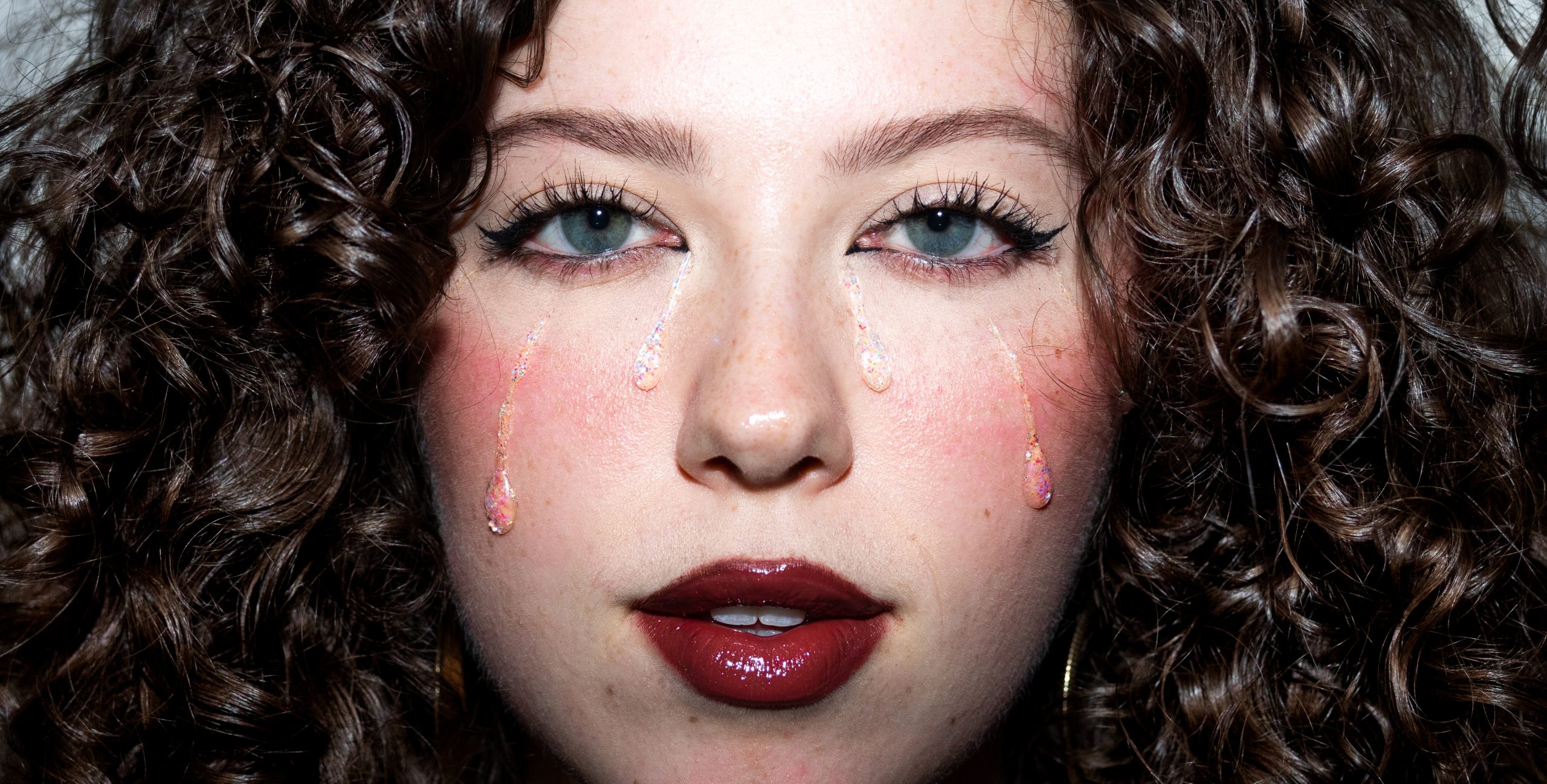 Close-up portrait of Phoebe Rea with glitter tears. Photo by Tessa Libby.