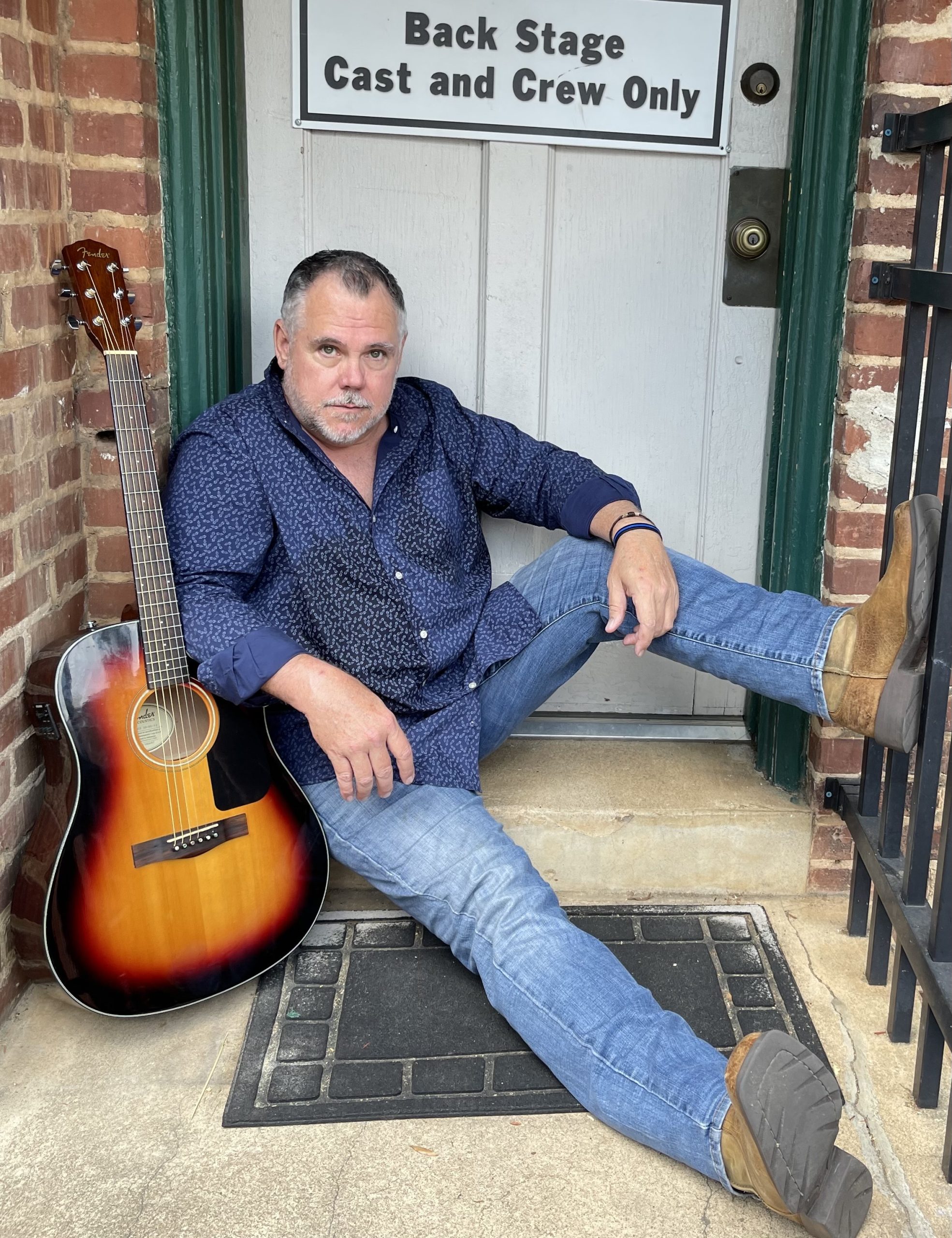 Tim Counts seated with his acoustic guitar outside a backstage entrance